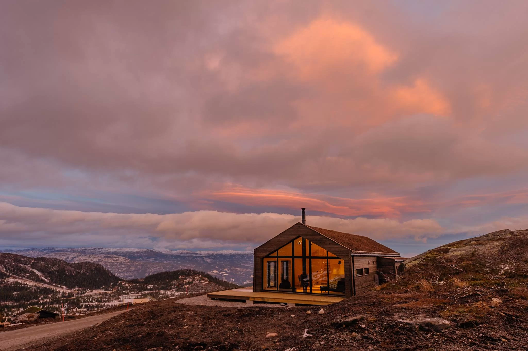 Liten hytte med store vinduer og rosa himmel.