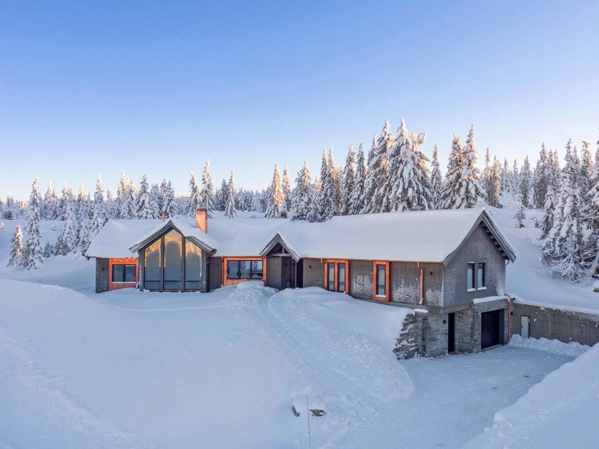 Snødekket hytte i skogen med blå himmel.