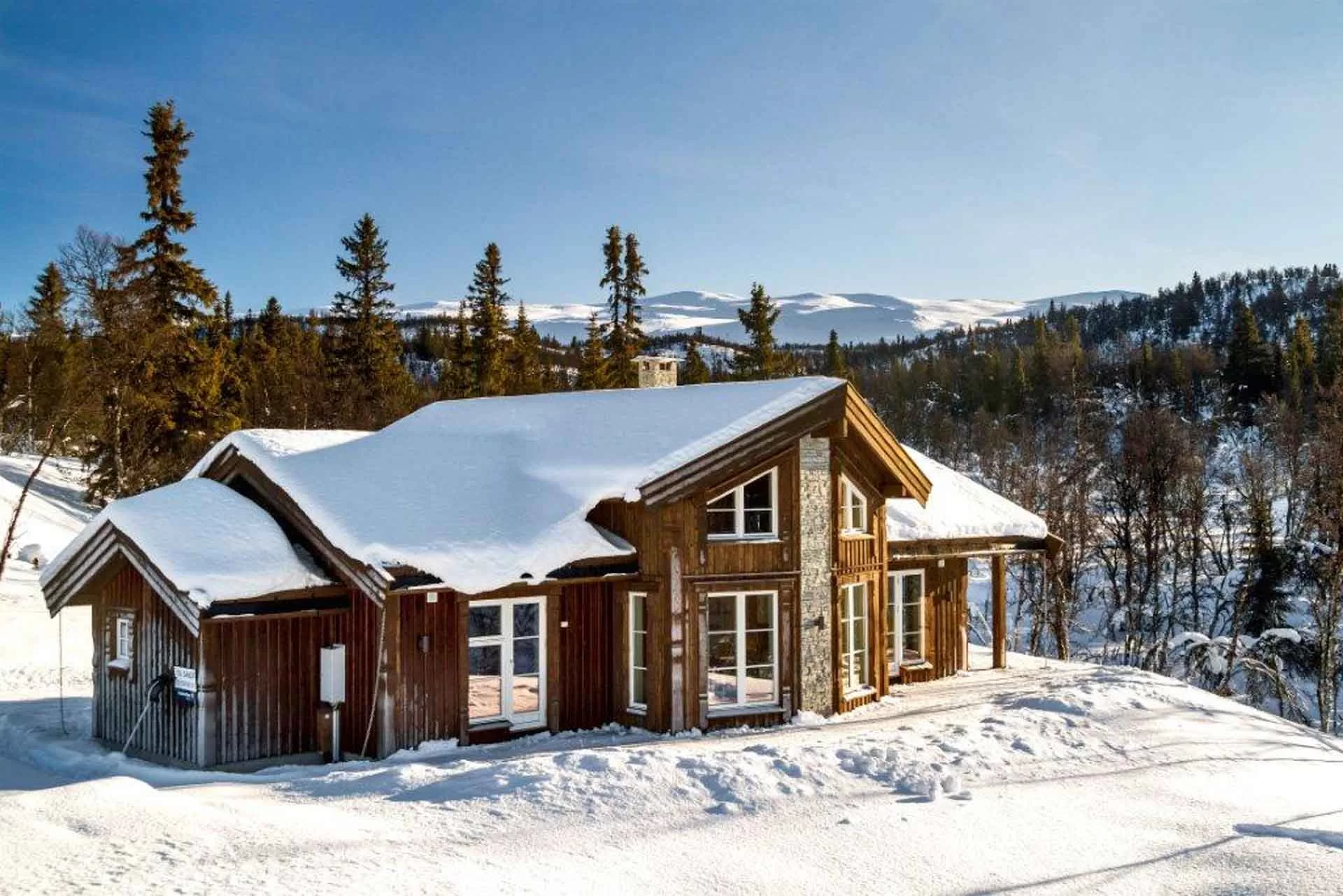 Brun trehytte i vinterlandskap med fjellutsikt.